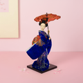Traditional Japanese doll in a blue kimono with an umbrella on a pink background