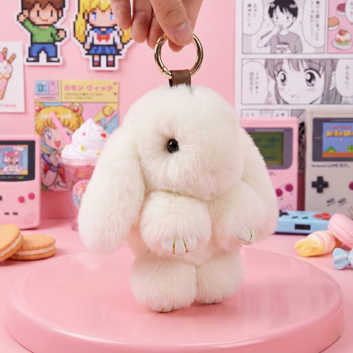 White fluffy bunny keychain held by a hand against a pink background with cartoon characters and vintage toys.