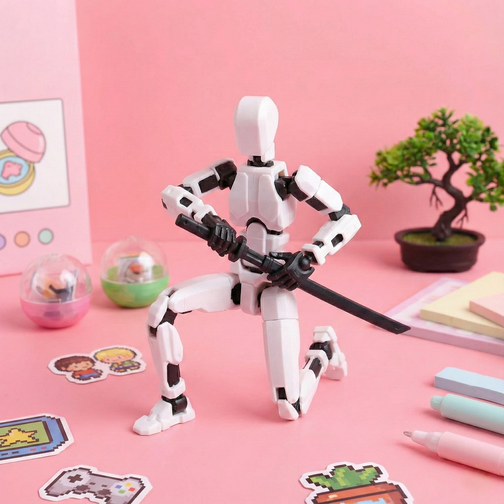 White robot figurine with black accents on a pink background with stationery items.