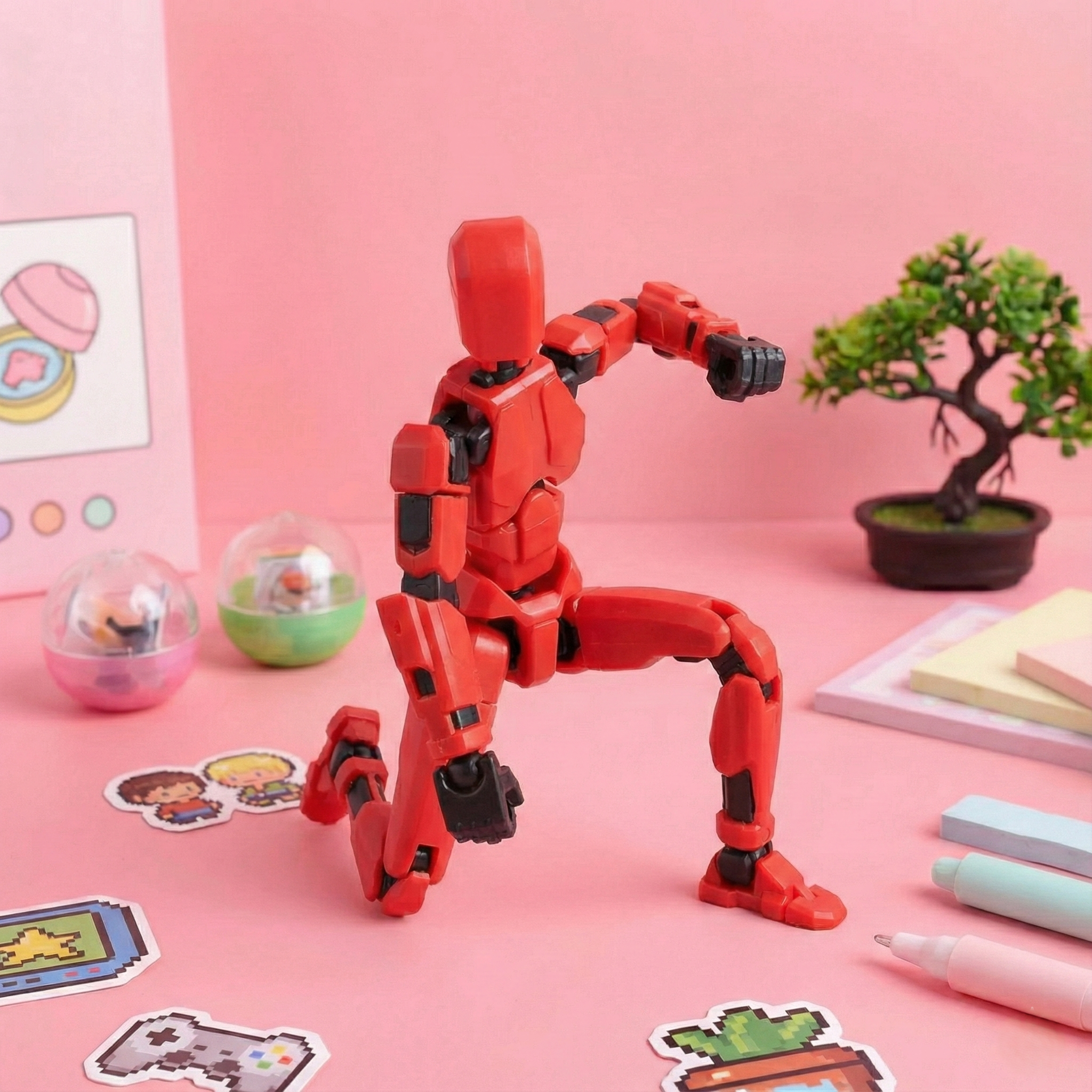 Red robot toy on a pink surface with stationery items and a small plant.