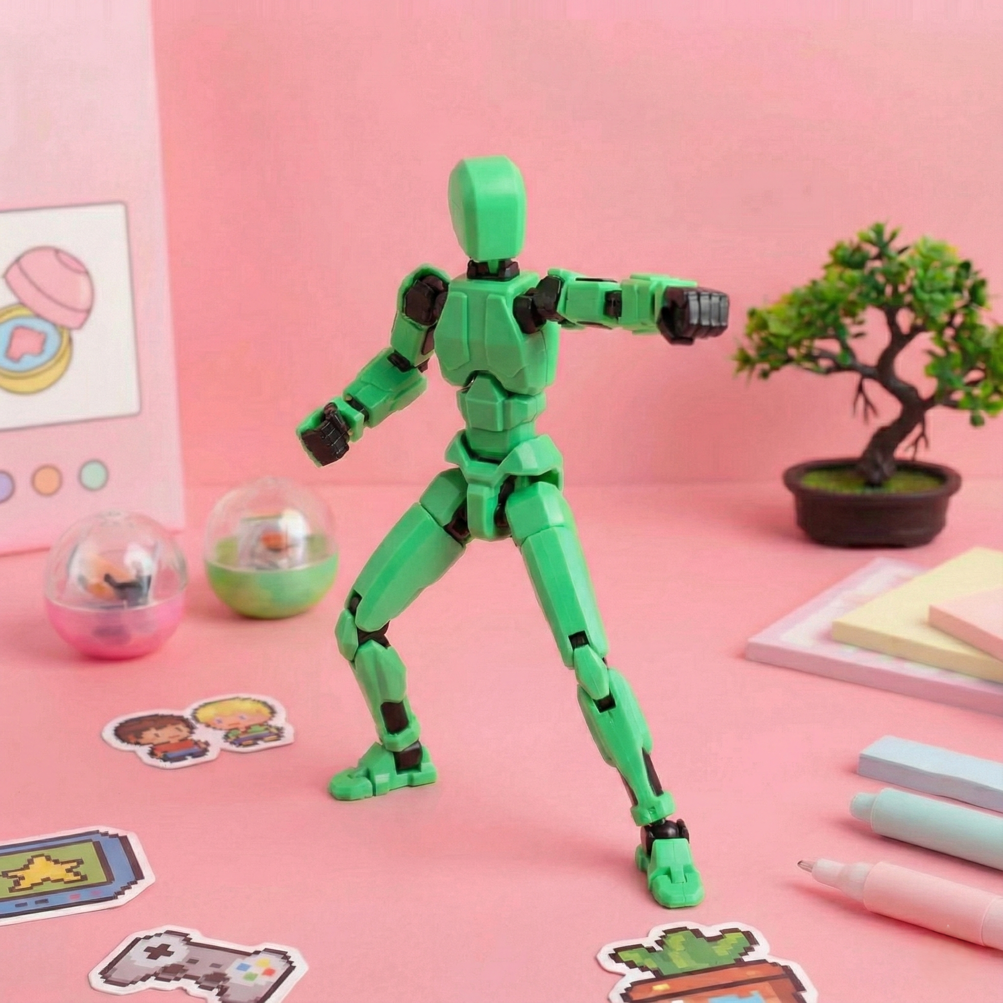 Green robot toy on a pink surface with stationery items